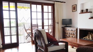 Un salón con una silla de madera, un televisor, una chimenea y vistas a través de un ventanal.