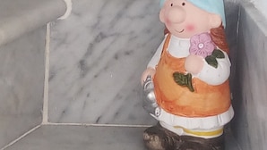 Pieni tonttipatsas istuu laatoitetun lattian kulmassa.
