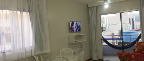 Habitación con una mesa de comedor, sillas, televisor, ventilador de techo y vista a un edificio.