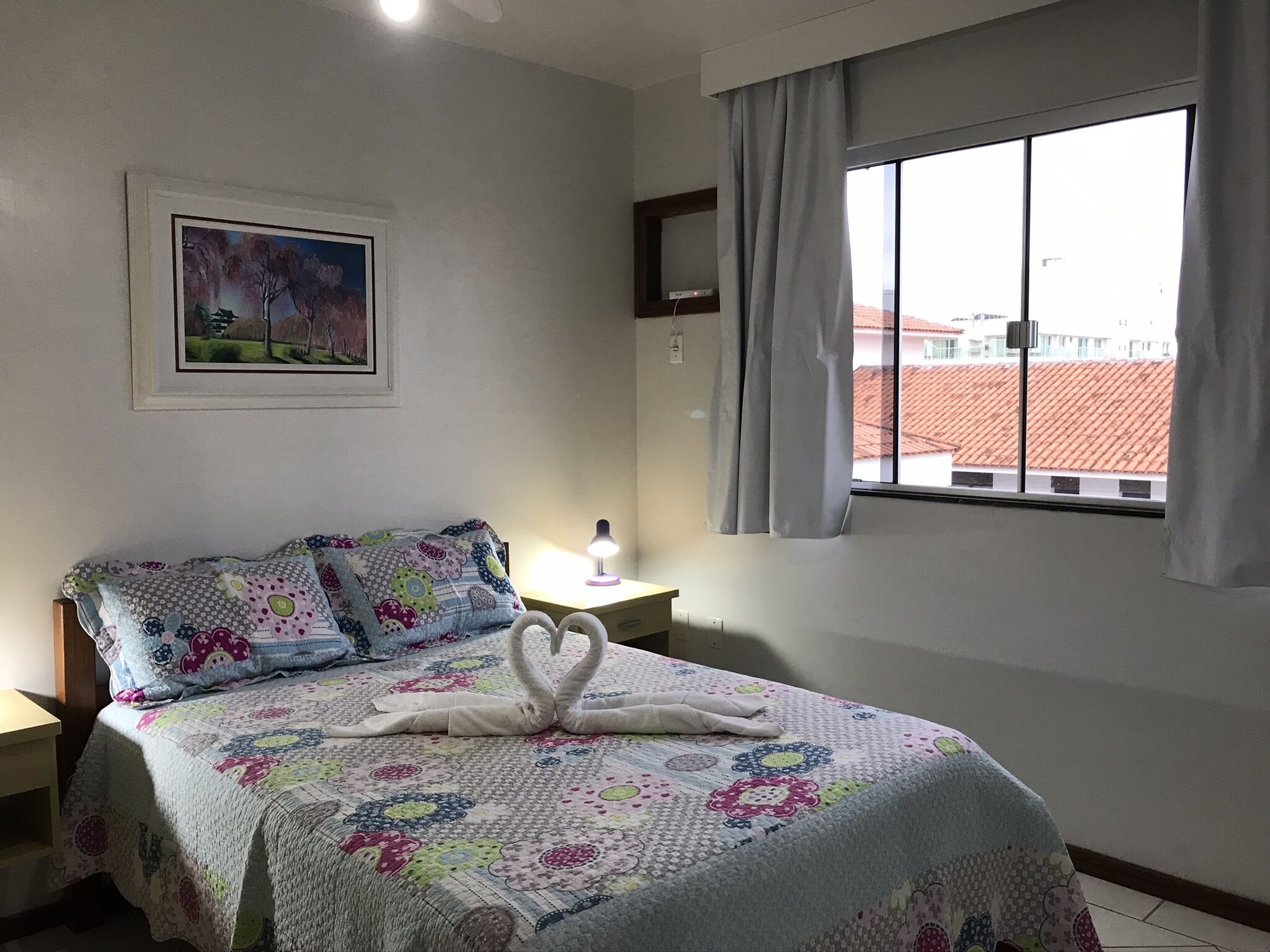Ein ordentlich bezogenes Bett mit einem floralen Quilten, einer Nachttischlampe und einem Bild an der Wand.