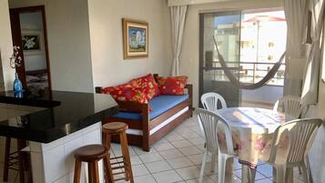 Un espacio habitable compacto con kitchenette, un sofá con cojines rojos, una mesa de comedor con sillas y un ventanal con cortinas.