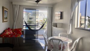 A room with a bed, a desk, a chair, a table, a hammock, and a view of buildings through a window. - KASATO MARU RESIDENCE (Florianópolis)