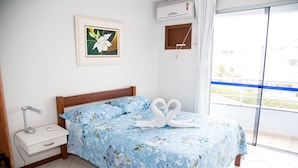 A bedroom with a bed, a nightstand, a wall-mounted air conditioner, a window with a view, and a framed picture on the wall. - KASATO MARU RESIDENCE (Florianópolis)