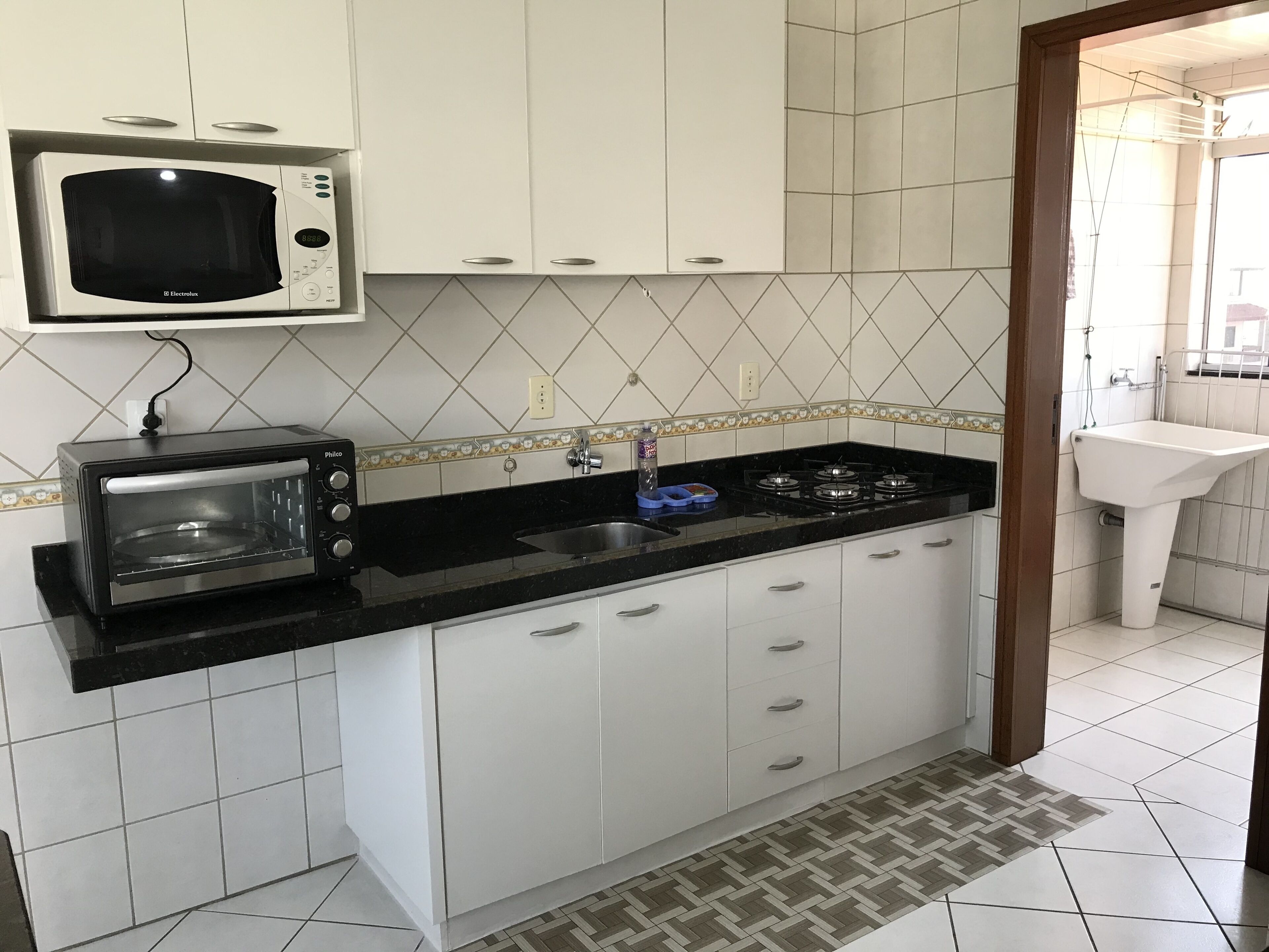 Une cuisine avec des meubles blancs, un plan de travail noir, un four à micro-ondes, un grille-pain et une cuisinière à gaz.