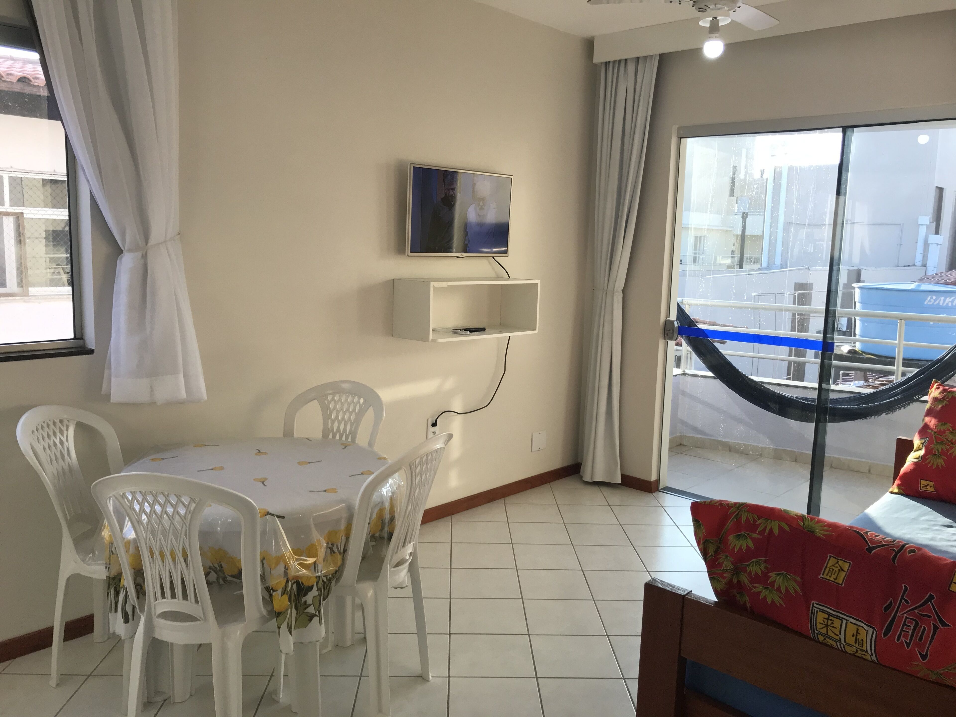 A room with a dining table, chairs, a TV mounted on the wall, a hammock, and a view of the outside.