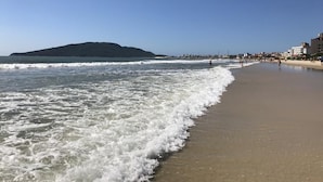 A beach with waves, a distant hill, and buildings along the shore. - KASATO MARU RESIDENCE (Florianópolis)