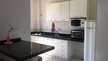 Una cocina con armarios blancos, encimera negra, microondas y refrigerador.