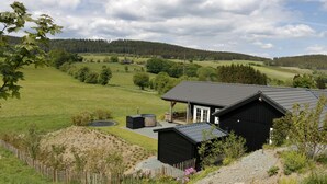 Una casa rural con fachada negra, camino de grava y jardín vallado.