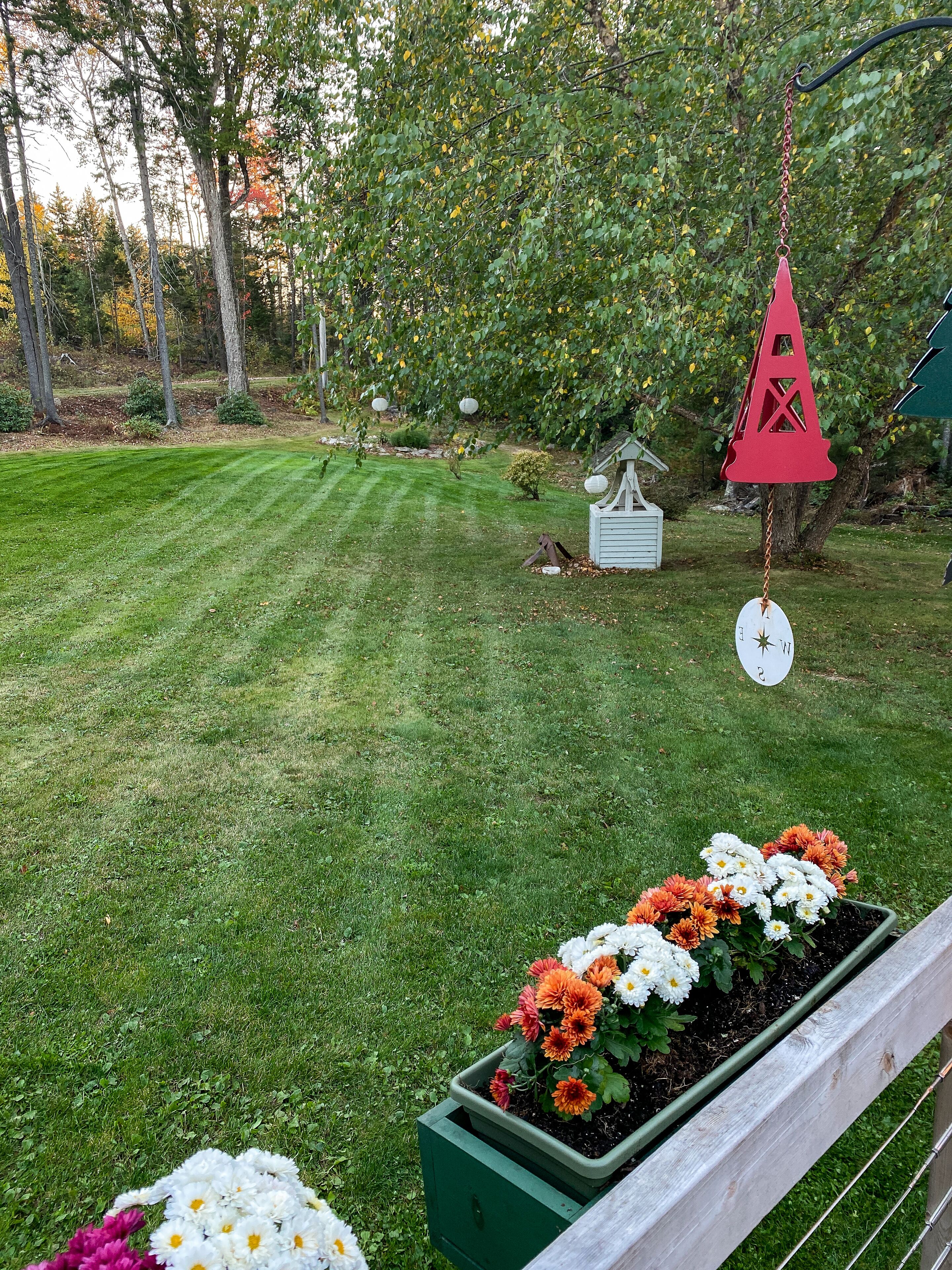 A well-maintained garden with a wooden fence, a hanging bird feeder, and a small white structure.