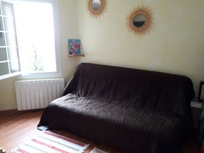 Een kamer met een bank met bekleding, een radiator, een raam met zonwering en twee spiegels aan de muur.