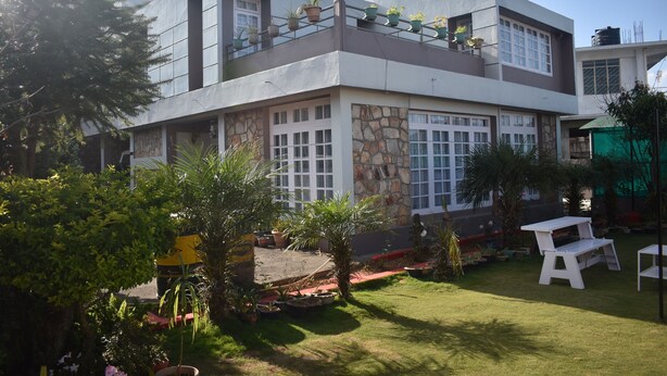 Una casa moderna de dos pisos con fachada de piedra, ventanas amplias y un balcón con plantas en macetas.