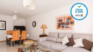 Een moderne woonkamer met een bank, een glazen salontafel en een eetgedeelte met stoelen en een tafel.
