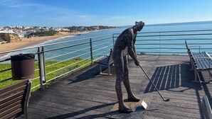 Een sculptuur van een figuur op een houten terras met uitzicht op een strand en de oceaan.