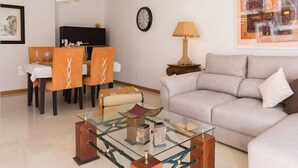Een moderne woonkamer met een bank, een glazen salontafel en een eetgedeelte met stoelen en een tafel.