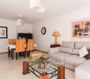 A modern living room with a sofa, a glass coffee table, and a dining area with chairs and a table.