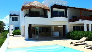 A modern two-story building with a pool, large windows, and a thatched roof. - Iz Cay Luxury Ocean Front Villa (Progreso)