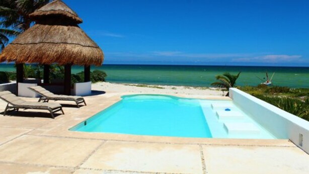 A pool area with lounge chairs, a thatched-roof structure, and a view of the ocean. - Iz Cay Luxury Ocean Front Villa (Progreso)