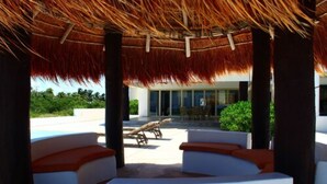 A covered outdoor seating area with white cushioned benches and a thatched roof. - Iz Cay Luxury Ocean Front Villa (Progreso)