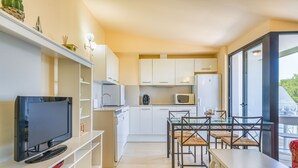 A modern kitchen with white cabinets, a dining table with chairs, a flat-screen TV, and a large window offering a view of greenery. - BEAUTIFUL DUPLEX IN CALA SANTANDRIA-CIUTADELLA WITH POOL AND WIFI (Cala Santandria-Ciutadella-Islas Baleare)