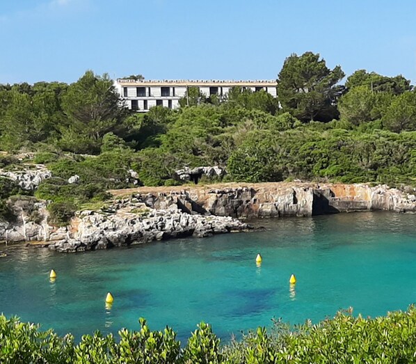 A coastal hotel with a rocky shoreline, clear turquoise water, and lush greenery.