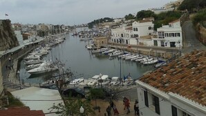 A marina with boats docked, buildings along the waterfront, and a pedestrian walkway. - BEAUTIFUL DUPLEX IN CALA SANTANDRIA-CIUTADELLA WITH POOL AND WIFI (Cala Santandria-Ciutadella-Islas Baleare)