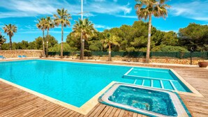 A swimming pool with a wooden deck, surrounded by palm trees and a stone wall. - BEAUTIFUL DUPLEX IN CALA SANTANDRIA-CIUTADELLA WITH POOL AND WIFI (Cala Santandria-Ciutadella-Islas Baleare)