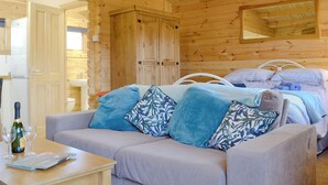 A cozy wooden cabin room with a sofa, a bed with striped bedding, and a wooden wardrobe.
