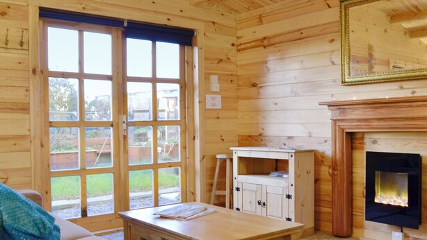 A wooden interior with a sofa, a small table, a fireplace, and a window with a view of the outside.