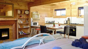 A cozy cabin interior with a bed, a fireplace, a dining area, and a kitchen.