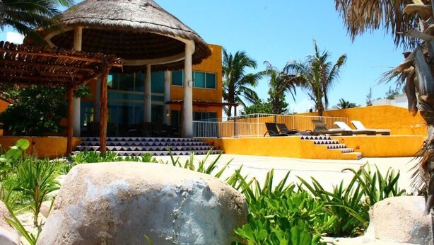 Un resort con un pabellón de techo de paja, un área de piscina con sillones de descanso y exuberante vegetación tropical.