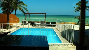 A swimming pool with a view of the ocean, surrounded by palm trees and a covered area with lounge chairs. - Uinic Chay Luxury Ocean Front Villa (Progreso)