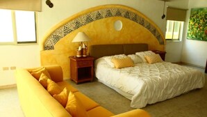 Un dormitorio con una cama, un sofá amarillo y una mesita de noche con una lámpara.