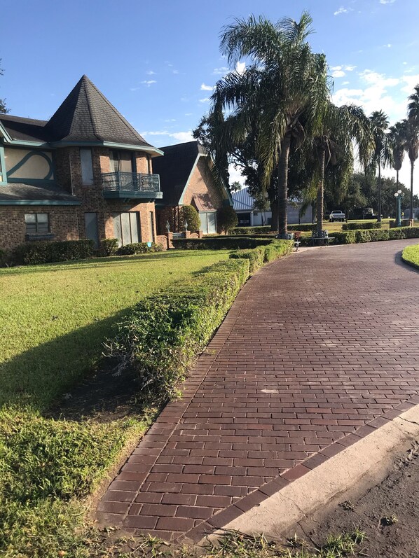 A brick pathway leading to a building with a green roof and a balcony. - El Castillo (The Castle) (McAllen)