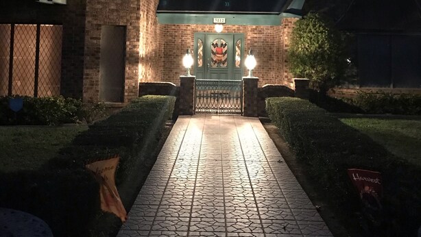A brick building with a tiled entrance pathway leading to a gated area with two wall-mounted lights. - El Castillo (The Castle) (McAllen)