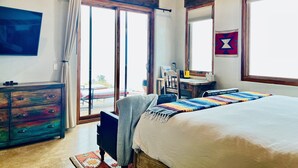 A bedroom with a large bed, a desk with a chair, a television, and a ceiling fan.