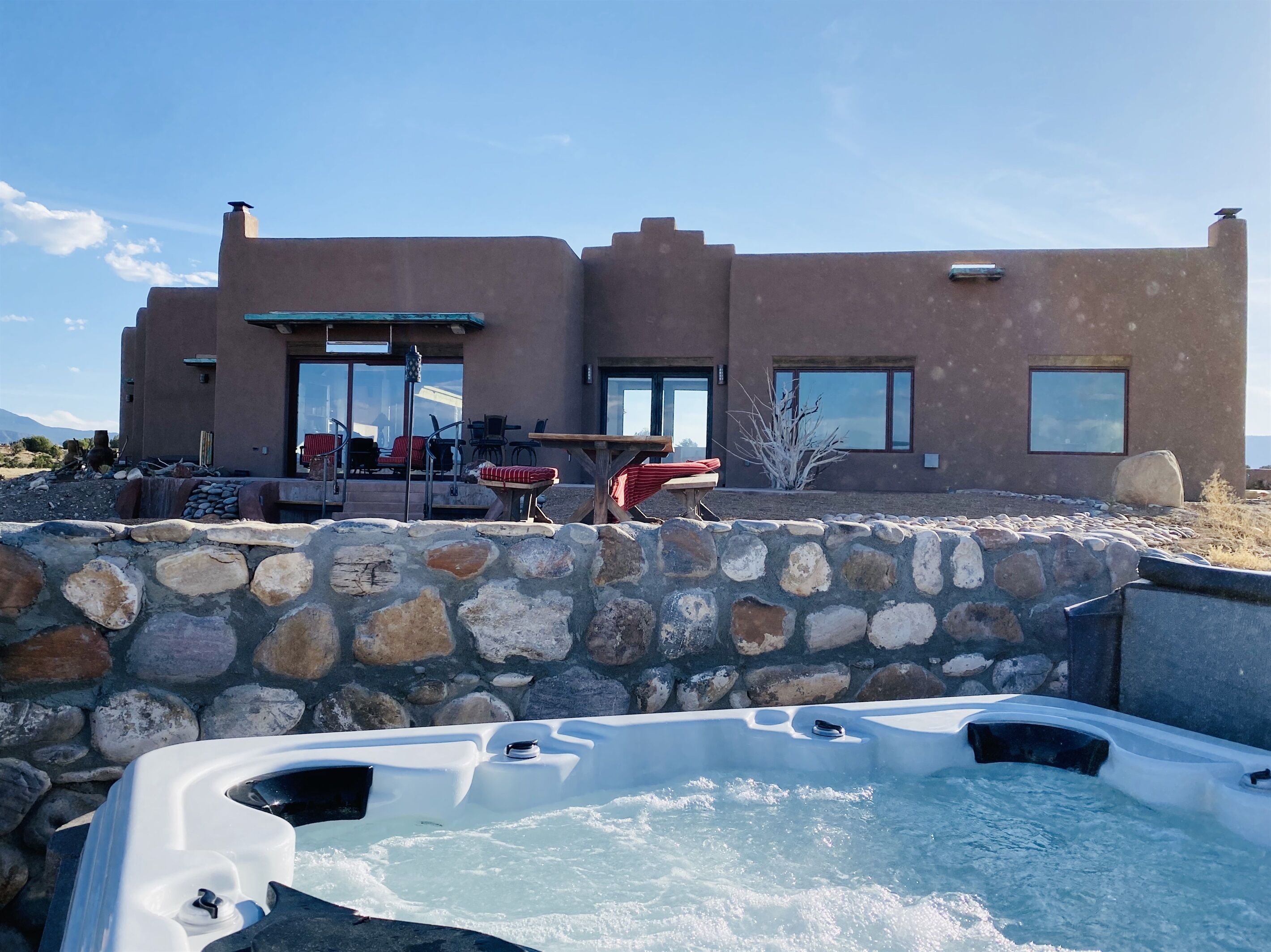 A modern house with a stone wall and a hot tub in the foreground.