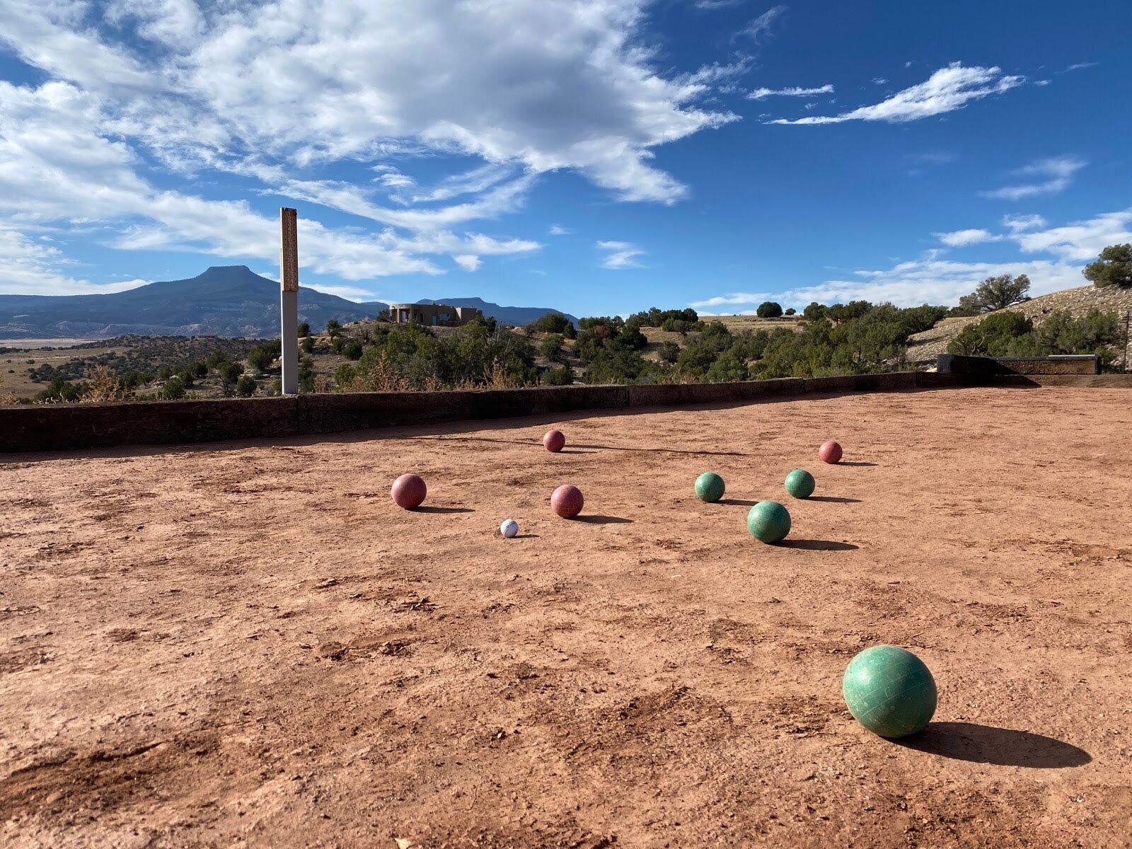 An outdoor area with a dirt ground, several sports balls, and a distant view of a mountain and buildings.