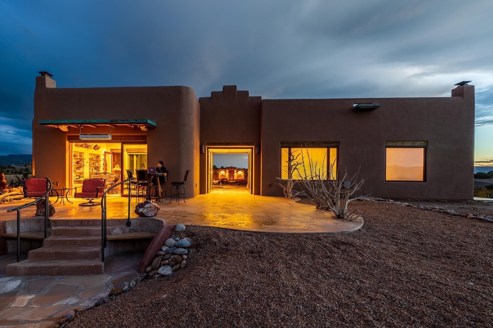 A modern house with a patio, outdoor seating, and a view of the interior.