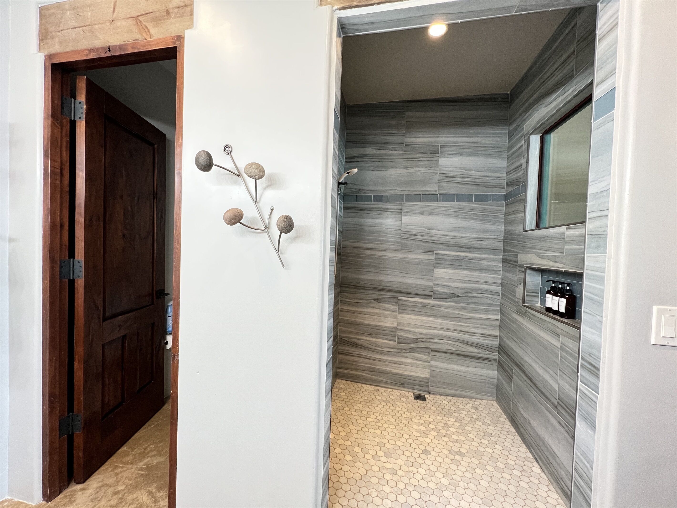 A bathroom with a shower, a wooden door, and a wall-mounted sink.