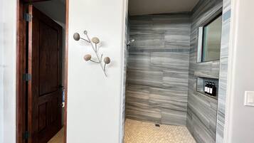A bathroom with a shower, a wooden door, and a wall-mounted sink.