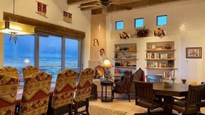 A dining area with a large table and chairs, a ceiling fan, and a view of the ocean through large windows.