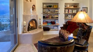 A living room with a fireplace, bookshelves, a sofa, and a view of a snowy landscape.