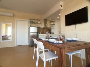A compact kitchen with a built-in refrigerator, white cabinets, and a dining area with a wooden table and white chairs.