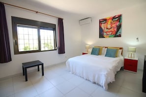 A bedroom with a bed, bedside tables, a bench, a window with curtains, and a painting on the wall.
