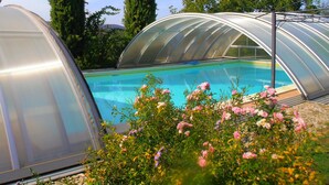 Una piscina con una estructura de invernadero transparente, rodeada de follaje y flores.