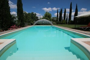 Une piscine surmontée d’un pont de verre, entourée de grands arbres et bordée d’un ciel dégagé.