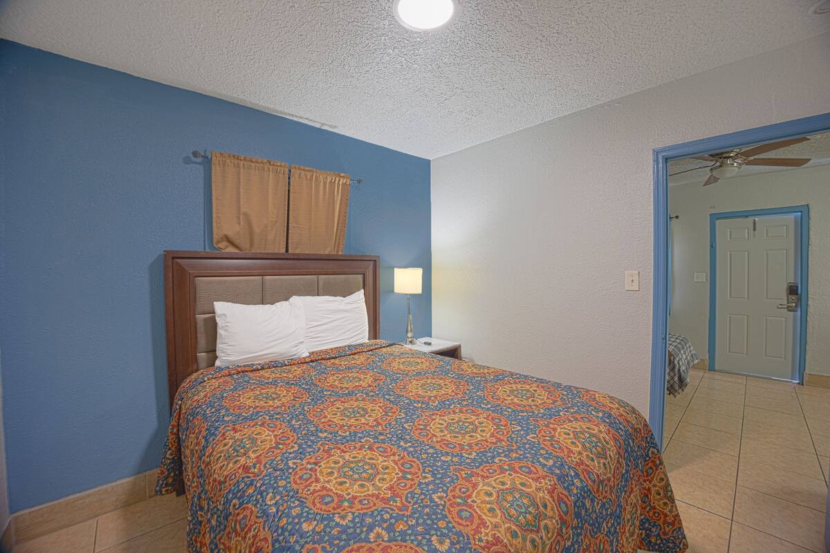 A bedroom with a bed, a nightstand, a lamp, a ceiling fan, and a door leading to another room.
