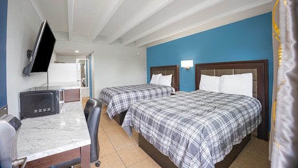 A hotel room with two beds, a desk, a TV, and a bathroom visible through an open door. - Aladdin Motel By OYO Merritt Island (Merritt Island)