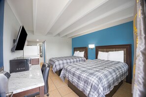 Quarto de hotel com duas camas, uma escrivaninha, uma televisão e banheiro visível por uma porta aberta.