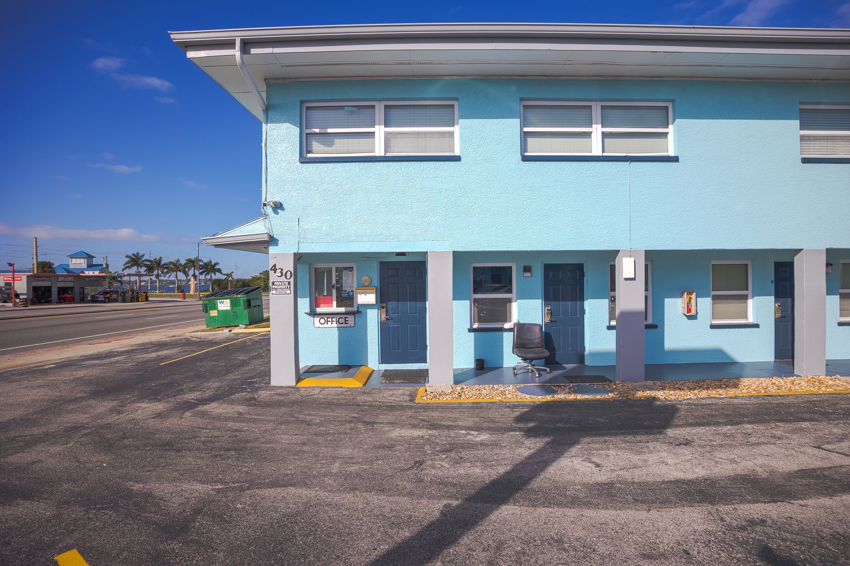 A two-story building with a blue exterior, a small porch, and a sign indicating an office.